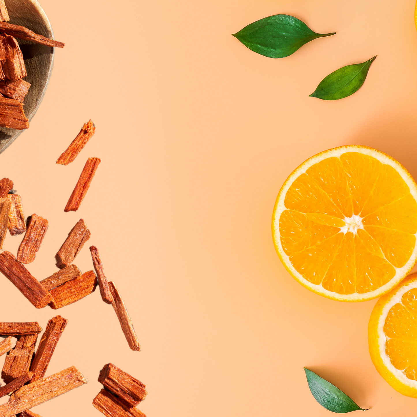 Cinnamon sticks, orange slices, and green leaves on a peach-colored background